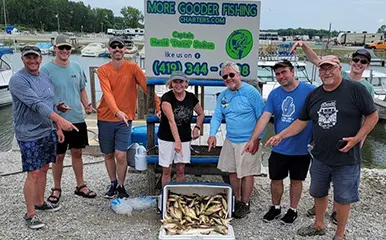 Eight smiling anglers display their catch in front of More Gooder Fishing Charters sign at a Lake Erie marina on July 28, 2023.