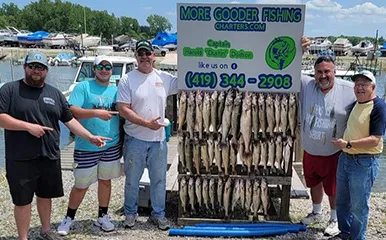Group of five anglers proudly displaying their fishing success with More Gooder Fishing Charters, posing behind a rack full of fish at a marina on May 29, 2023.