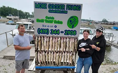 Happy group at More Gooder Fishing Charters displaying an impressive catch of fish on a rack at Lake Erie docks, with promotional sign visible, on July 11, 2023.