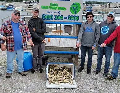 Happy anglers with a cooler full of perch after a successful outing with More Gooder Fishing Charters, with contact information sign in the background.