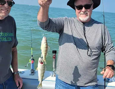 Two joyful fishermen with a freshly caught perch on a More Gooder Fishing Charters boat during a successful outing.