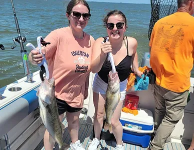 Two joyful women showcasing their walleye catch on a sunny day with More Gooder Fishing Charters, reflecting a successful and enjoyable fishing trip.